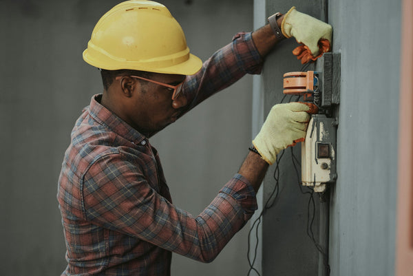 Electrician in hard hat and insulated gloves working on a wall-mounted electrical unit