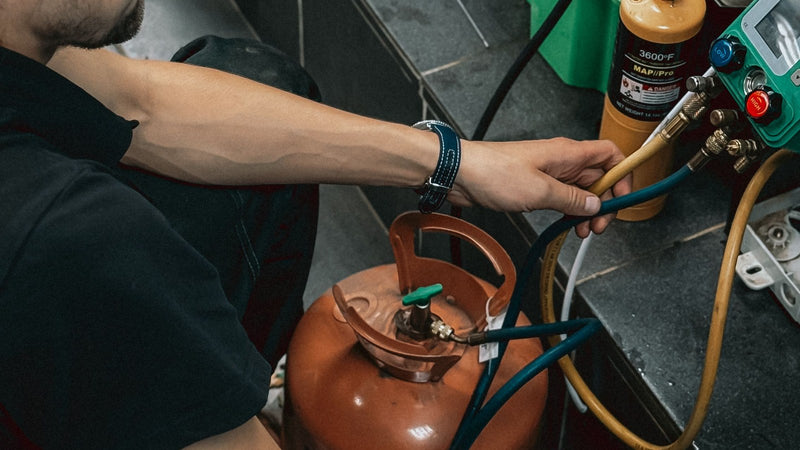 Technician working with refrigerant cylinders and gauges in a workshop