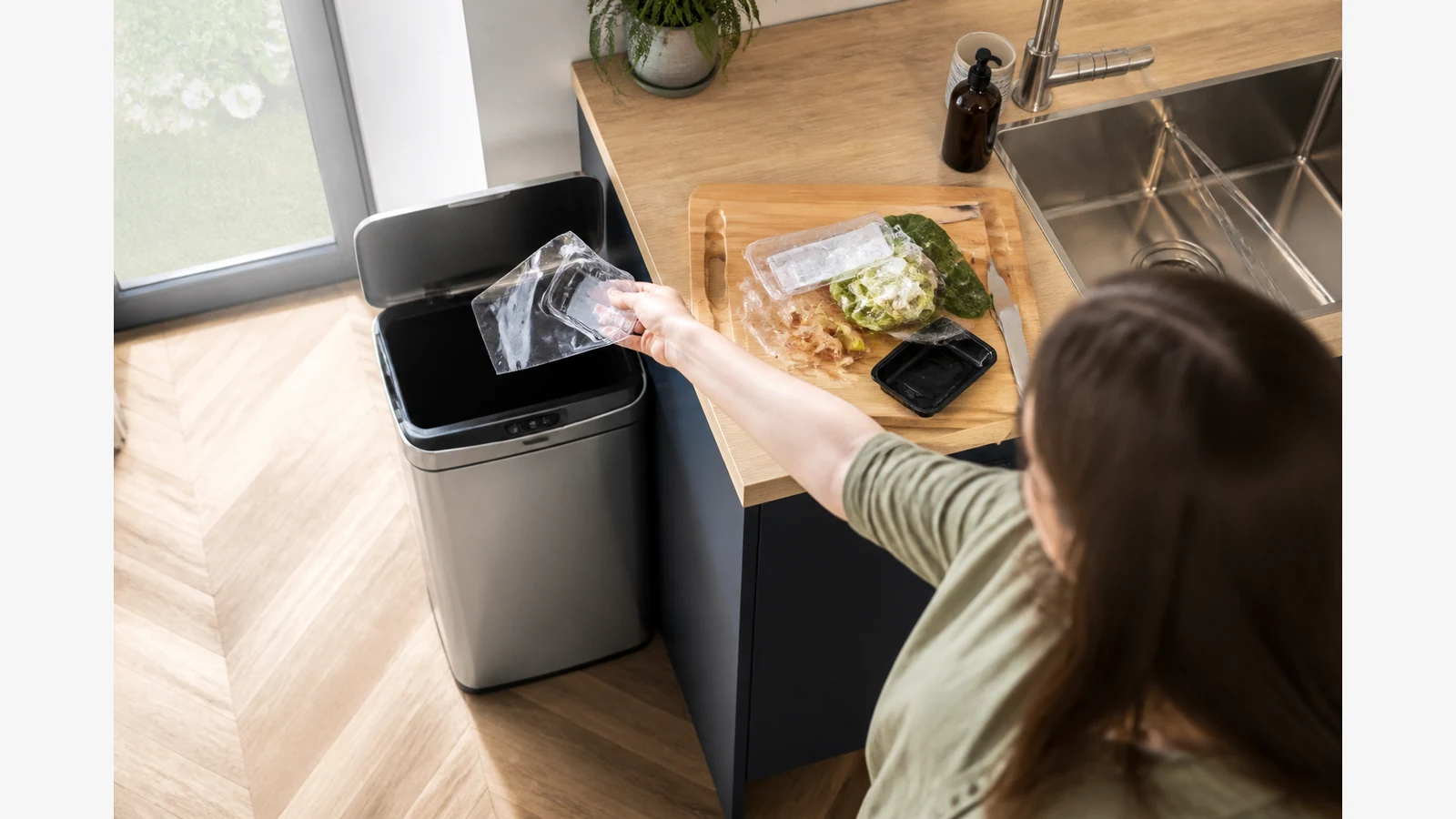 Touchless stainless kitchen bin opening beside a prep board during raw-meat tidy-up