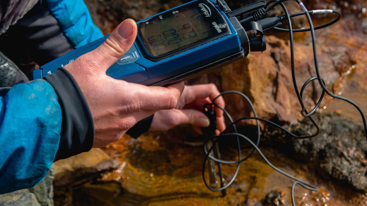 Researcher measuring stream water with a handheld pH meter