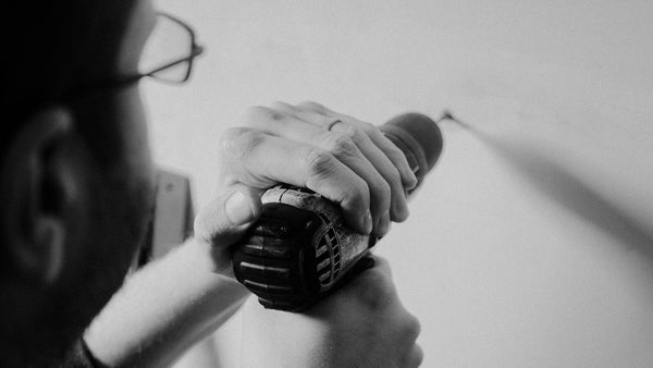 Person scanning a plasterboard wall with a stud finder and marking the stud position in pencil before drilling