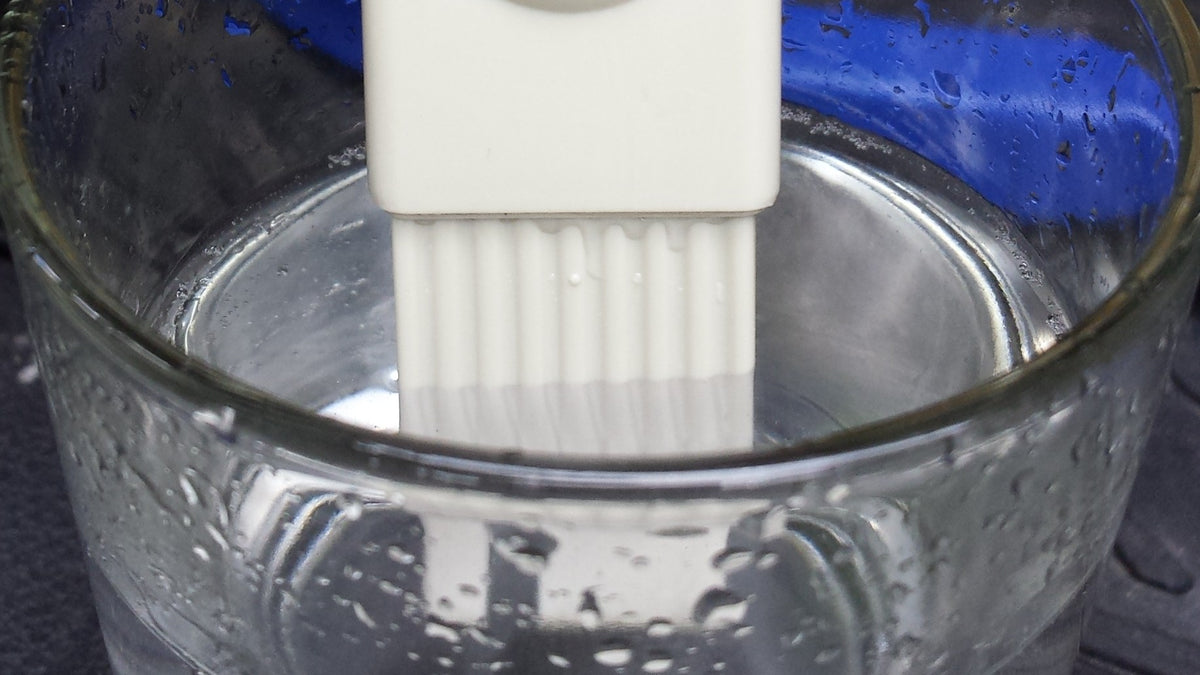 Person dipping a TDS meter into a glass of tap water at a kitchen sink to check the ppm reading